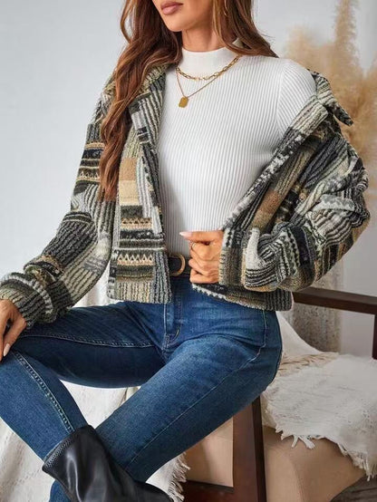 Woman wearing a patterned jacket, white sweater, and blue jeans sitting on a chair.