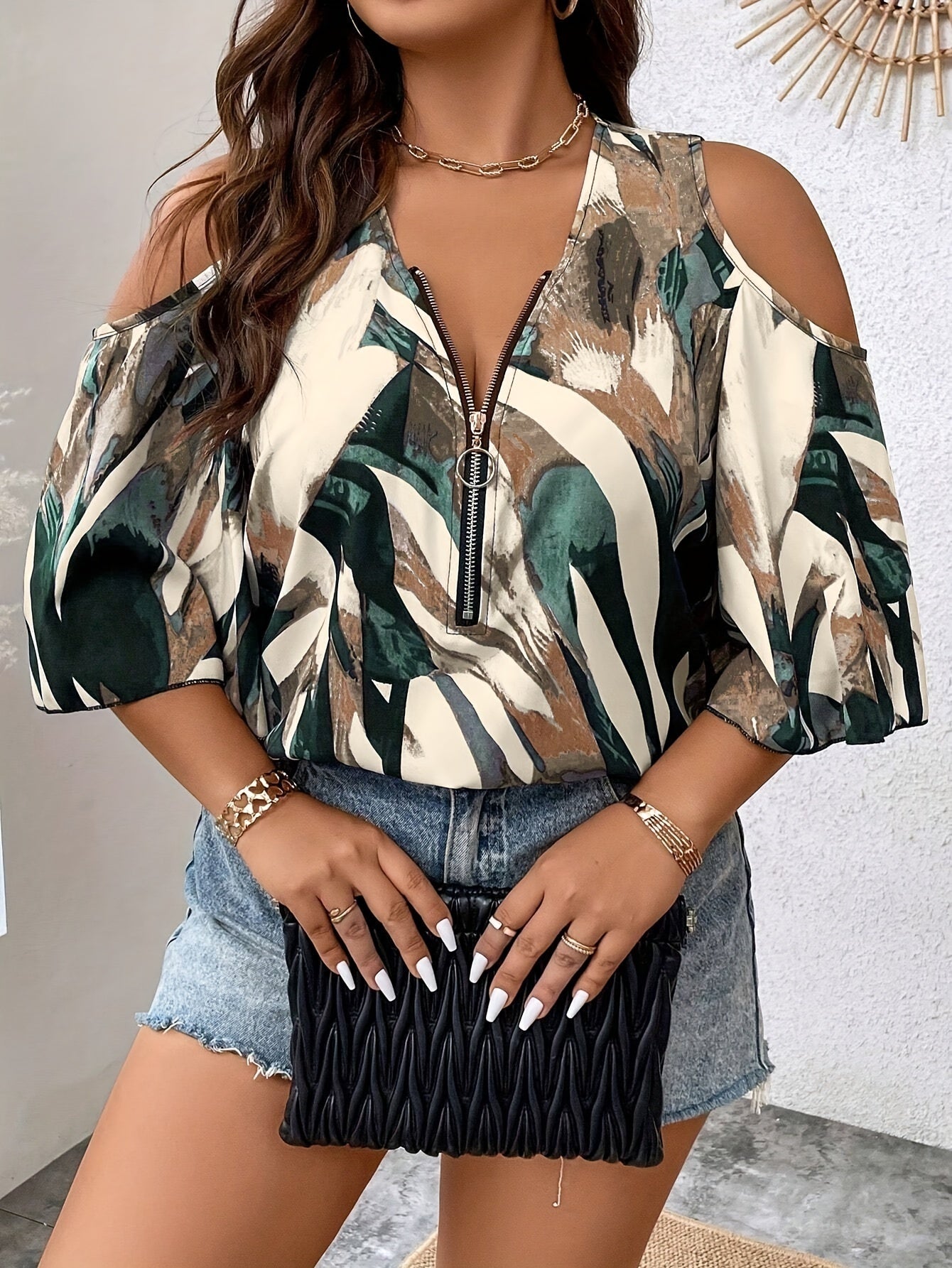 Woman wearing a patterned blouse with denim shorts and holding a black clutch.